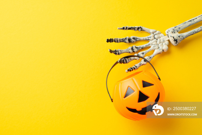 Halloween concept. Top view photo of skeleton hand holding pumpkin basket for trick-or-treat on isol