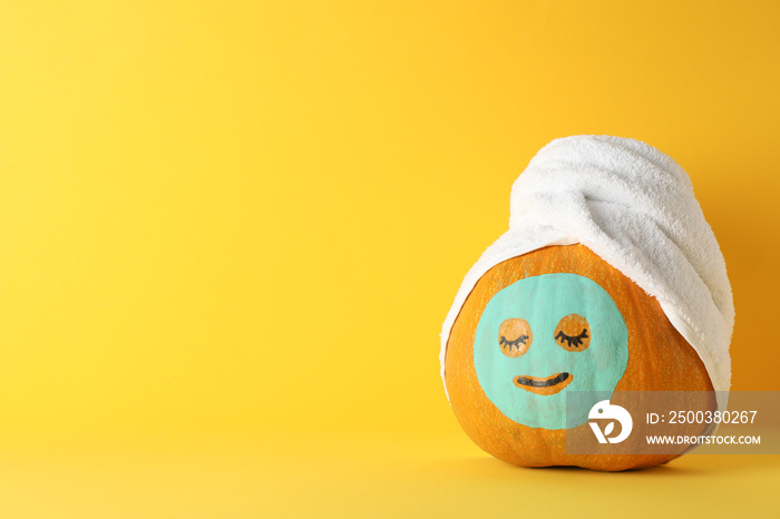 Pumpkin with facial mask and towel on yellow background, copy space