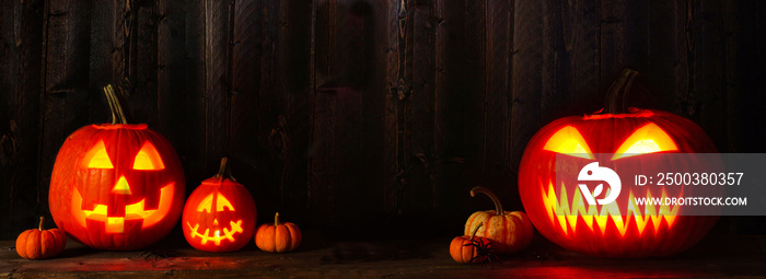 Halloween Jack o Lanterns at night. Banner with copy space against a dark wood background.