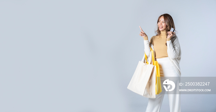 Panoramic shot of smiling woman holding credit card and shopping bags standing on light background. 