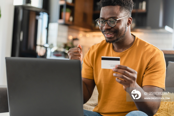 A young black cheerful man paying online with credit card