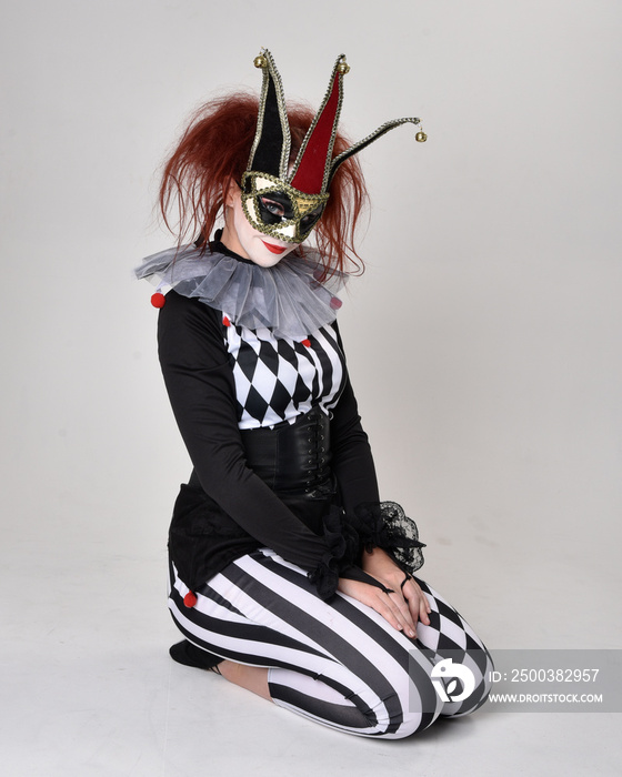 Full length  portrait of red haired  girl wearing a black and white clown jester costume, theatrical