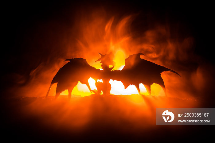 Silhouette of fire breathing dragon with big wings on a dark orange background