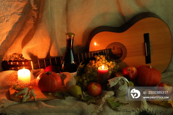 Wine and guitar. Apples, grapes and pears with pumpkins and leaves with candles flame standing on ta