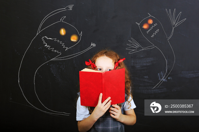 Child hiding behind the book, and is afraid near chalkboard. Edu