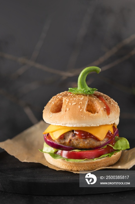 Halloween burger in a shape of pumpkin head jack o lantern on black. Scary cheeseburger on halloween