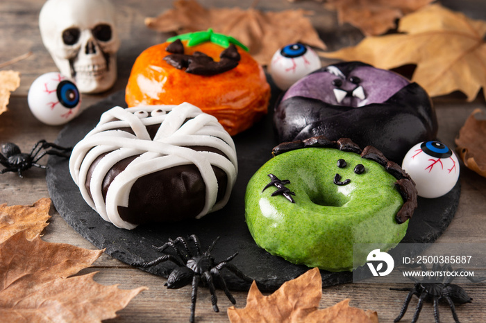 Assortmen of Halloween donuts and autumn leaves on wooden table