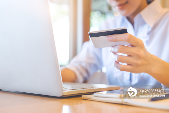 A womans hand holds a credit card and uses a laptop to shop online.