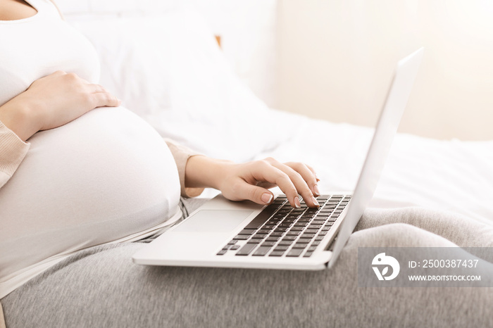 Pregnant woman browsing on laptop at home, side view, free space