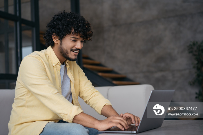 Young Indian freelancer copywriter working from home. Smiling handsome asian programmer using laptop