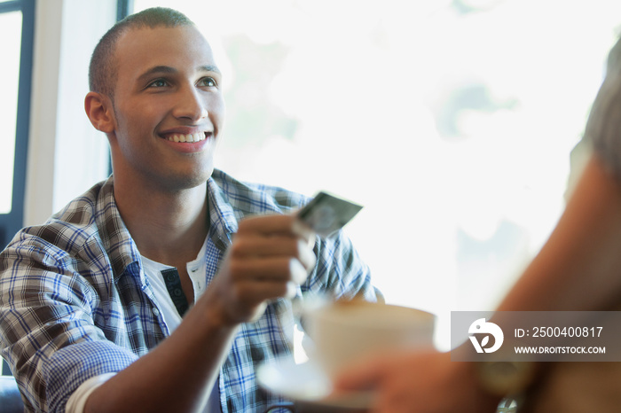 年轻成年男子在咖啡店将信用卡交给服务员