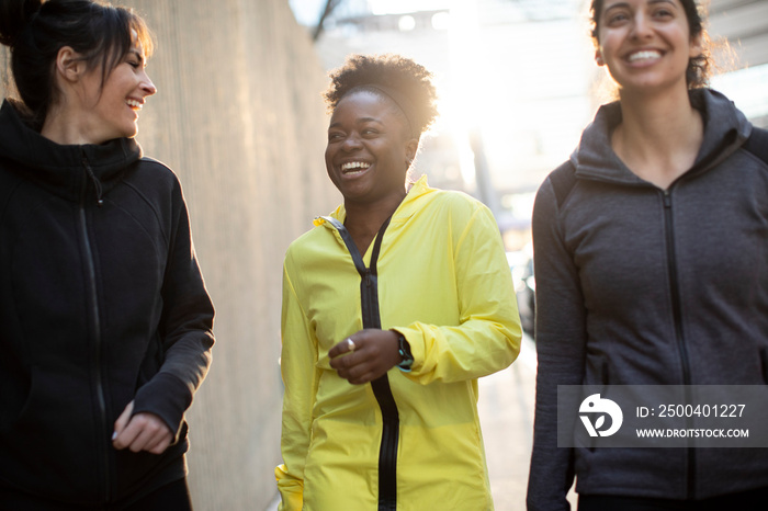 Happy confident female athletes talking while walking on sidewalk in city