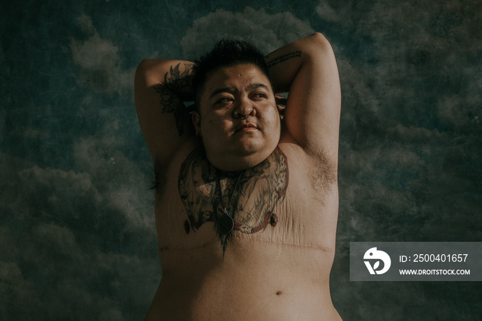 plus size non-binary person stretching arms behind head facing the sunlight with scars on chest