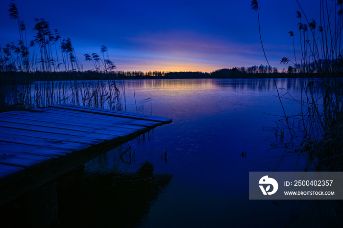 sunrise over wooden jetty and frozen lake