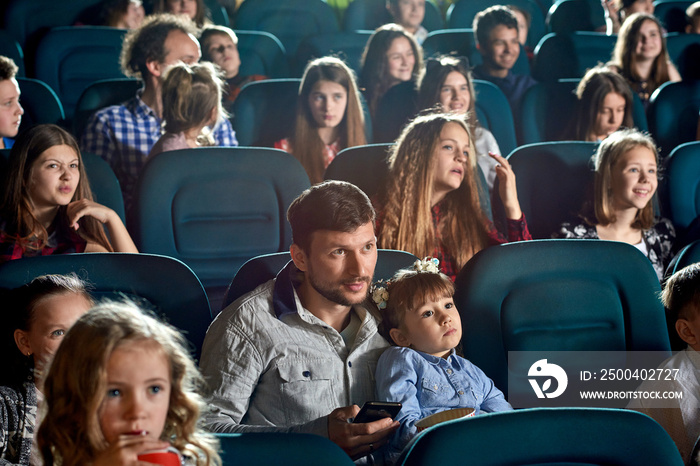 观众坐在电影院舒适的椅子上欣赏动画片。小女孩坐着
