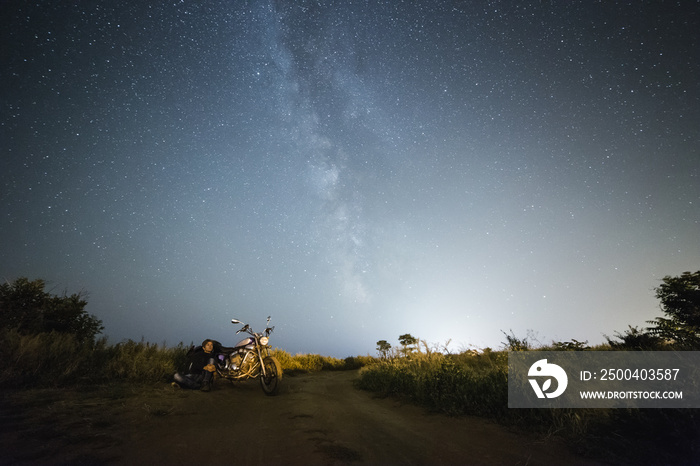 Young beautiful biker woman with motorcycle under stars of  home galaxy Miky Way. Female biker on fi