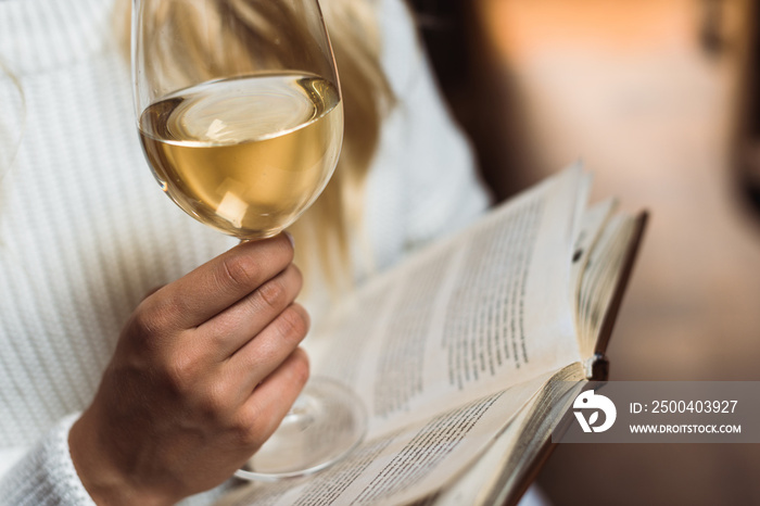 cropped view of young adult woman holding wine glass and book