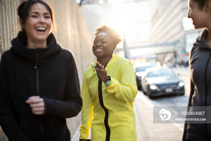 Happy confident female athletes talking while standing on sidewalk in city