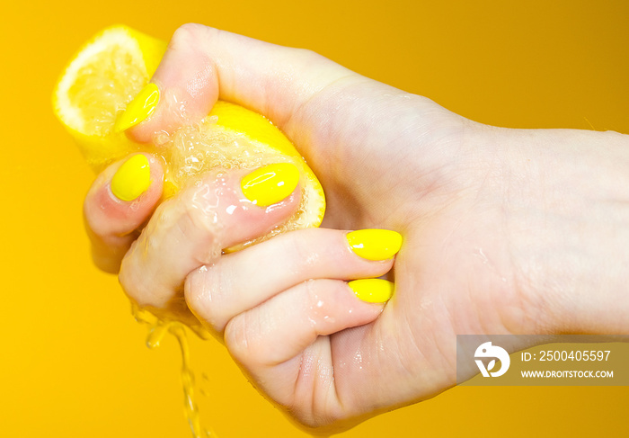 hand with yellow fingernails crushing a fresh, juicy lemon