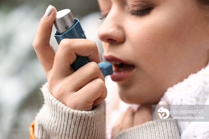 Young woman with inhaler having asthma attack outdoors, closeup