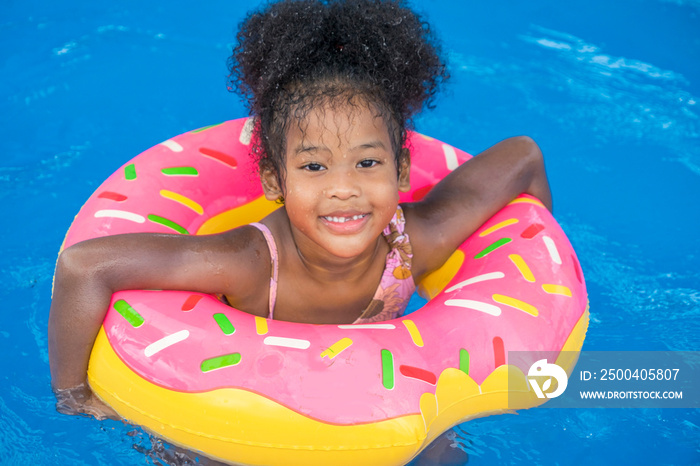 非裔美国女孩微笑快乐，在游泳池里玩得开心，游泳圈漂浮在水面上