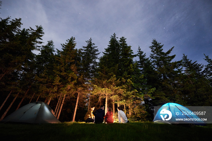 Evening camping near campfire against the backdrop of a powerful forest. Tourist people bask near th