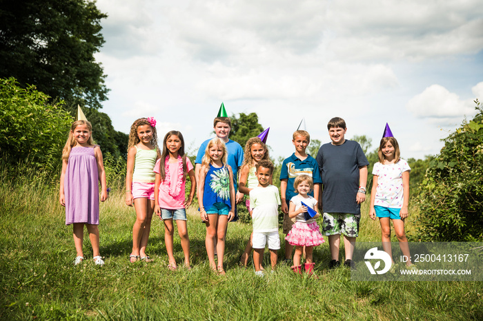 Children (2-3, 4-5, 8-9, 10-11) wearing party hats posing to photograph in meadow