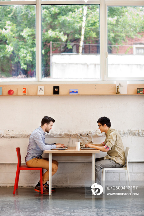 Two men using laptops at table