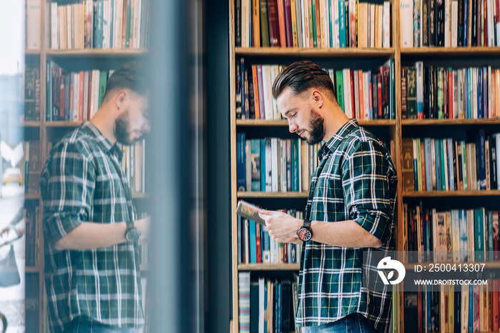 Side view of Caucasian male student in casual clothing reading best seller novel in public bookstore