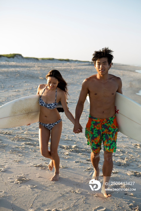 Asian-american couple carrying surfboards at beach