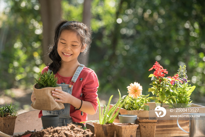 adorable asian little girl is planting spring flowers tree in pots in garden outside house, child ed