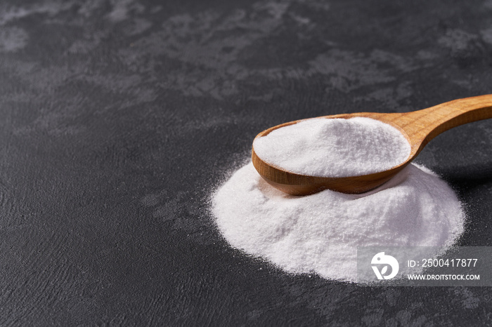 Sodium bicarbonate in a wooden spoon on a black background .