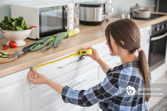 Young woman measuring furniture in kitchen