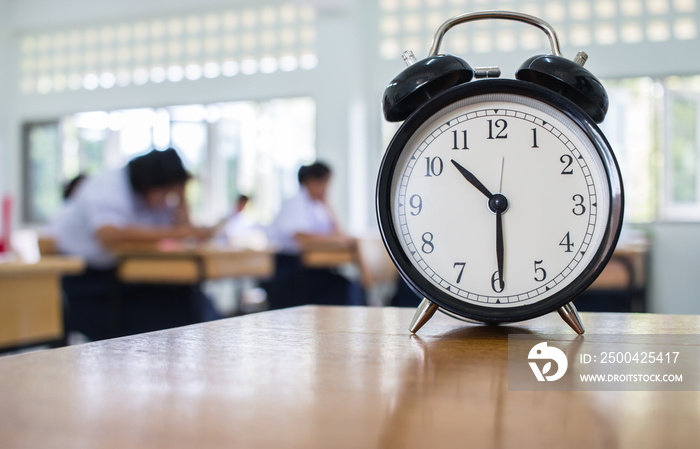 Closeup of Retro alarm clock with ten oclock on table teacher in blur students exams classroom. Tim