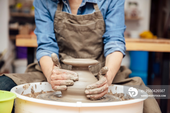 Senior female potter working on pottery wheel while sitting  in her workshop