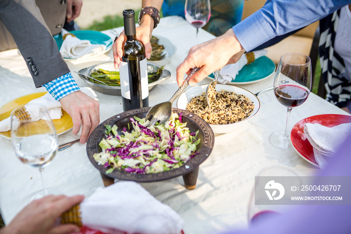 Cropped shot of adult friends helping themselves to food and drink at garden party table