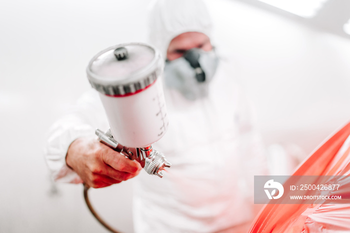 Portrait of automotive industry worker with spray gun with red paint painting a car in special booth