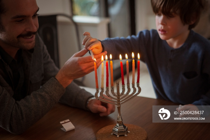 光明节期间，年轻人在家里引导儿子在烛台上点燃蜡烛
