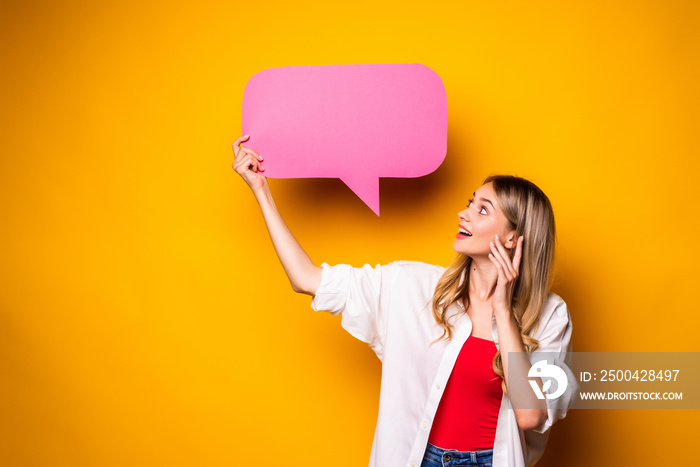 Portrait of a happy young woman holding empty speech bubble standing over yellow background