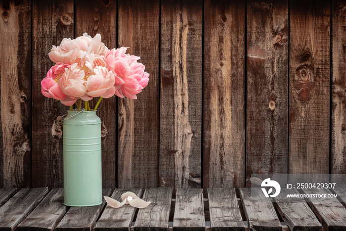 乡村木板桌左侧的绿色花瓶里放着一束粉色牡丹，为同事留出了空间