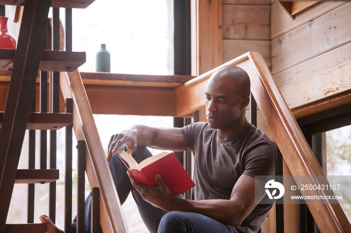 Man reading book while sitting on stairs at home