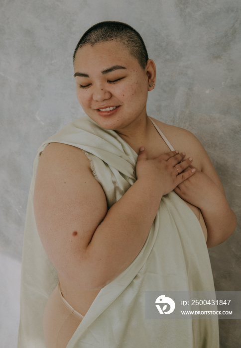 portrait of a plus size filipino woman with a shaved head looking down hands on heart holding satin 