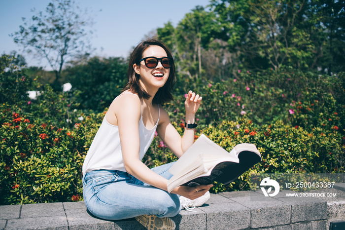 Young Asian woman in sunglasses with book smiling and looking at camera