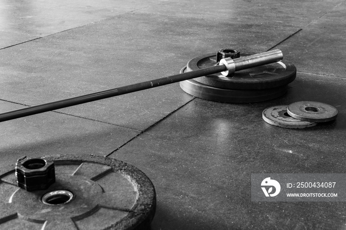 Barbell and weights on a gym floor, in black and white