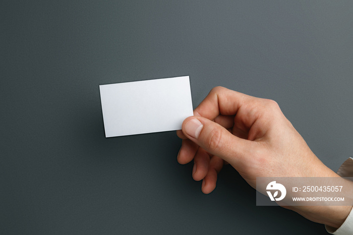 Male hand holding a blank business card on grey background for text or design. Blank credit card tem