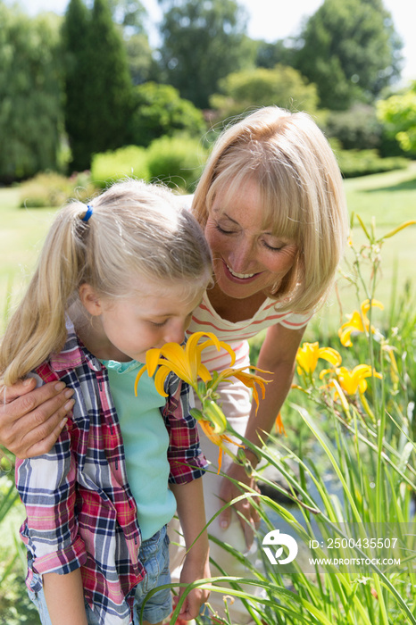 Grandmother and granddaughter smelling flowers in sunny garden