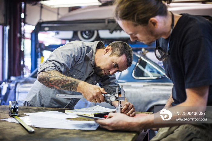 Mechanics measuring metal part in workshop