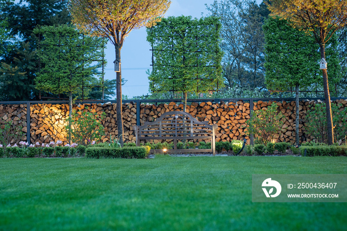 A modern form of a garden. Lanes of trees against the backdrop of a spectacular wooden fence. A benc