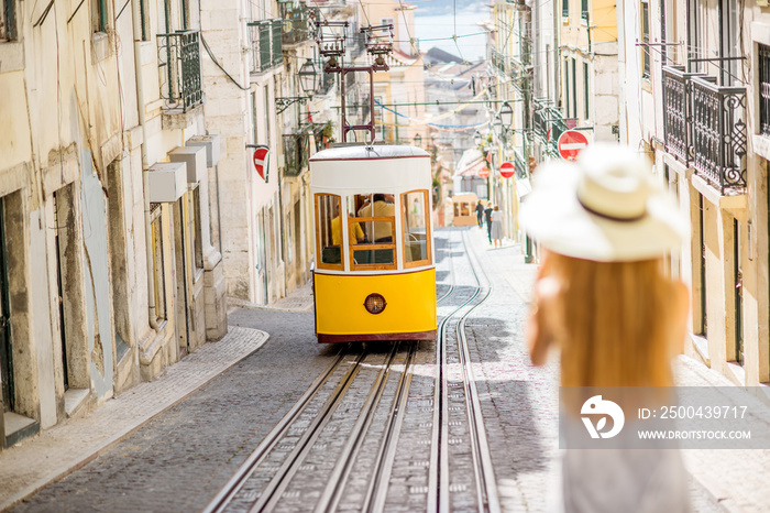 Young woman tourist photographing famous retro yellow tram on the street in Lisbon city, Portugal. W