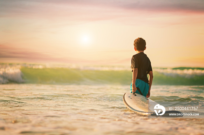 海滩日落，小冲浪男孩冲浪生活方式的后景放松拿着冲浪板看